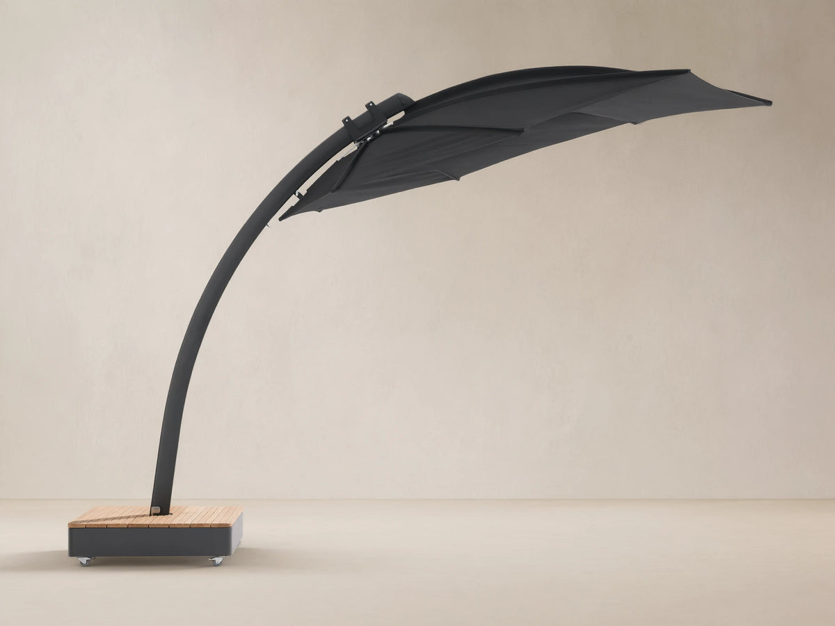 Black Icarus outdoor umbrella, open and tilted to the right, with a curved dark gray pole and a light wood-slatted base on wheels.