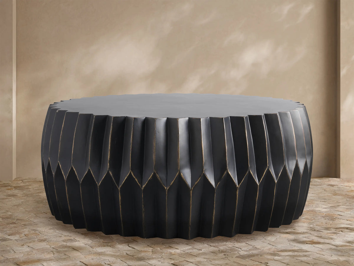 Round Indio Outdoor Coffee Table, dark gray, with pleated, faceted sides subtly highlighted in bronze, on a tiled floor.