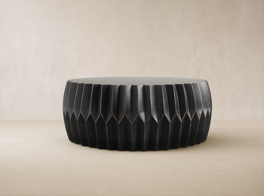 Round Indio Outdoor Coffee Table, dark gray, with pleated, faceted sides subtly highlighted in bronze, on a tiled floor.