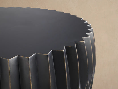 Round Indio Outdoor Coffee Table, dark gray, with pleated, faceted sides subtly highlighted in bronze, on a tiled floor.
