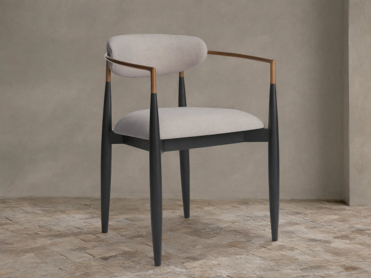 Jagger Outdoor Dining Arm Chair with black wooden frame, light grey cushions, and bronze-toned metal armrests, angled view.