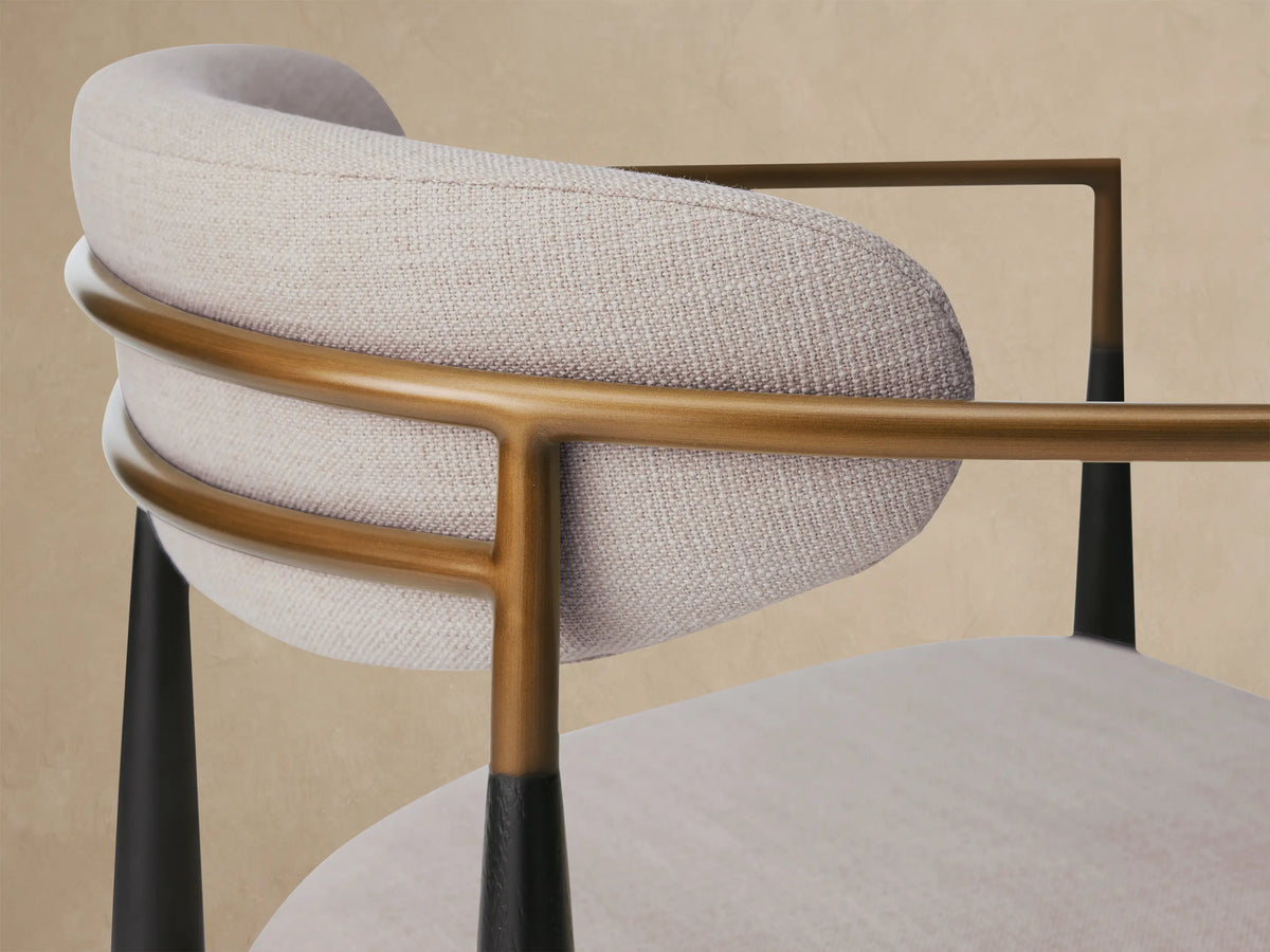 Jagger Outdoor Dining Arm Chair with light grey cushions, dark wood frame, light curved armrests, and brass accents, front view on tiled floor.