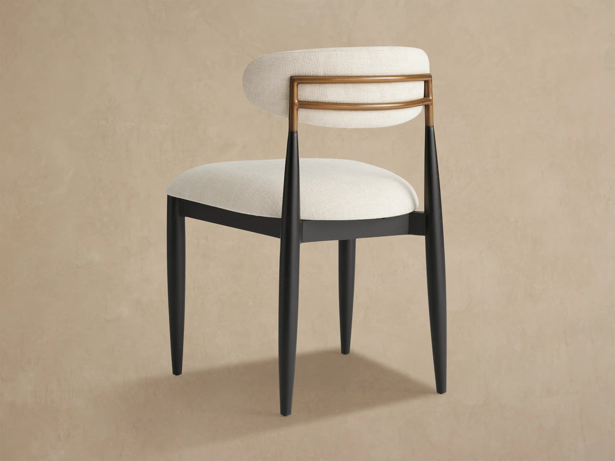 Close-up, angled view of Jagger Outdoor Dining Side Chair. Light fabric backrest with two curved golden teak slats and dark metal legs.