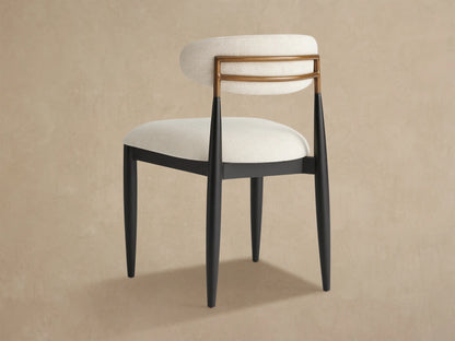 Close-up, angled view of Jagger Outdoor Dining Side Chair. Light fabric backrest with two curved golden teak slats and dark metal legs.