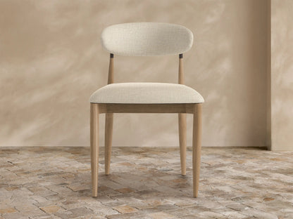 Front view of a light gray, textured Jagger Outdoor Collection Cover on a chair, with a front split, on a stone floor.