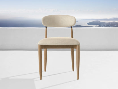 Jagger Outdoor Dining Side Chair, natural teak frame, light beige cushions, on a white patio overlooking a blue sea & islands.