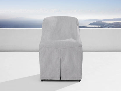 Jagger Outdoor Dining Side Chair, natural teak frame, light beige cushions, on a white patio overlooking a blue sea & islands.
