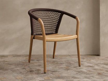 Kaia Outdoor Dining Chair with light teak wood frame & seat, brown woven rope backrest & armrests, on a stone floor.