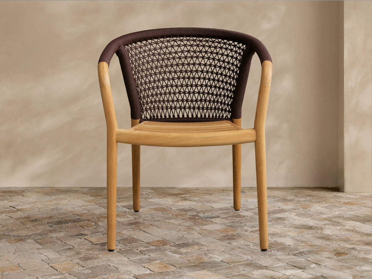 Kaia Outdoor Dining Chair with light teak wood frame & seat, brown woven rope backrest & armrests, on a stone floor.