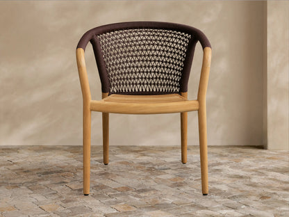 Kaia Outdoor Dining Chair with light teak wood frame & seat, brown woven rope backrest & armrests, on a stone floor.