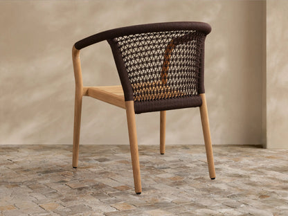 Angled close-up of Kaia Outdoor Dining Chair. Light teak wood frame and dark brown woven rope geometric backrest.