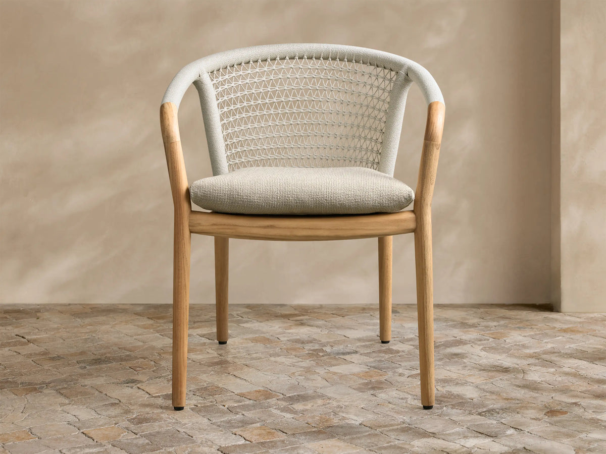 Stacked view of two Kaia Outdoor Dining Chairs with Cushion. Natural teak wood frames, light beige woven rope backs, slatted seats.
