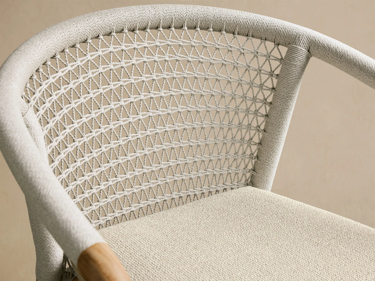Rear view of the Natural Teak Kaia Outdoor Dining Chair with a light grey cushion and woven back.