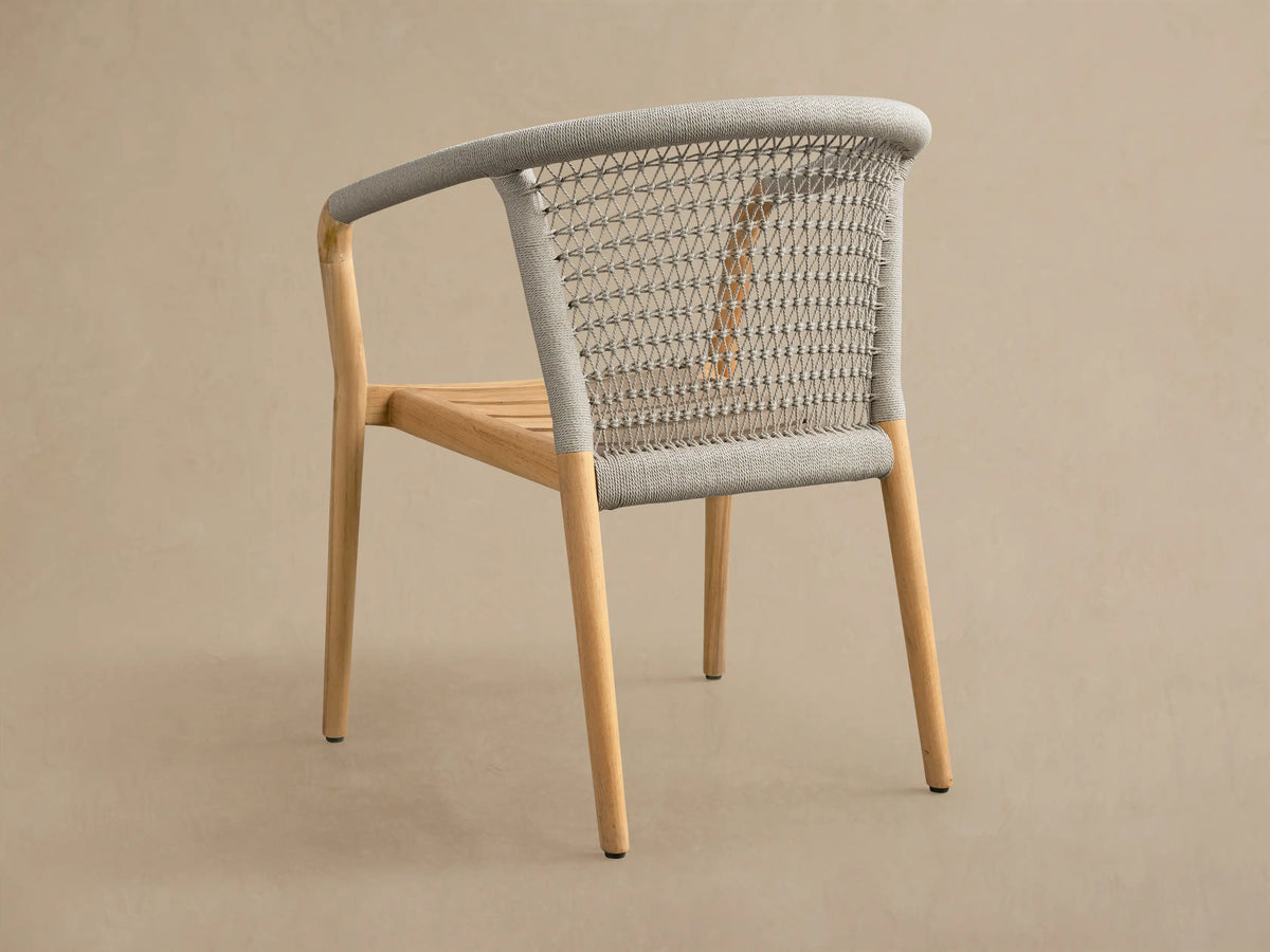 Rear-side view of natural teak Kaia Outdoor Dining Chair with light grey woven backrest and armrests.