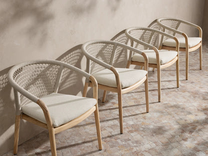 Four Kaia Outdoor Dining Chair with Cushion chairs with natural teak frames, light beige woven backs, and light beige cushions.