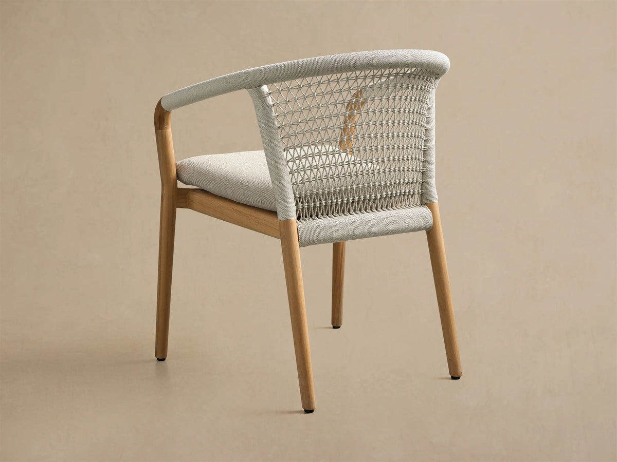 Rear view of the Kaia Outdoor Dining Chair with Cushion, featuring a natural teak wood frame, light grey woven back, and cushion.