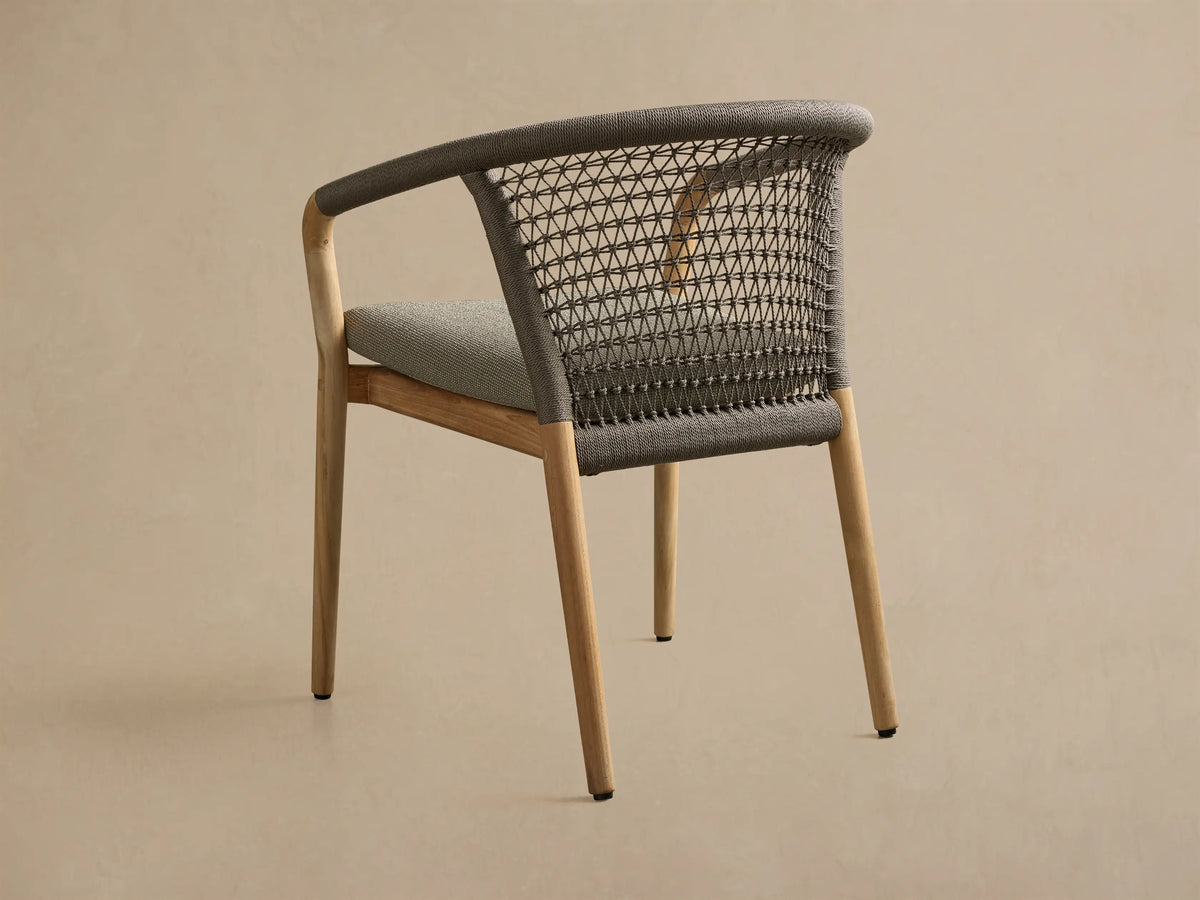 3/4 Rear-side view of the Kaia Outdoor Dining Chair with Cushion, featuring a natural teak frame and grey woven back and seat.
