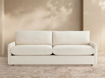 Front view of Kipton Outdoor Sofa, a two-seater with off-white cushions, on a patterned patio against a light beige wall.