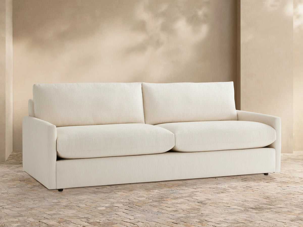 Front view of Kipton Outdoor Sofa, a two-seater with off-white cushions, on a patterned patio against a light beige wall.