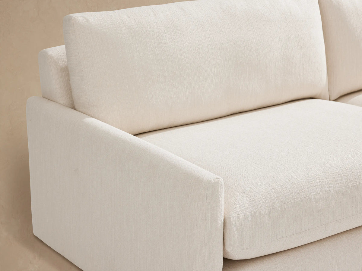 Off-white Kipton Outdoor Sofa with plush two-seat cushions and wide track arms, shown on a textured stone patio.