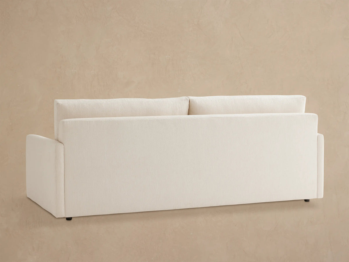 Close-up of Kipton Outdoor Sofa in cream textured fabric, showing an armrest, seat cushion, and backrest against a neutral wall.