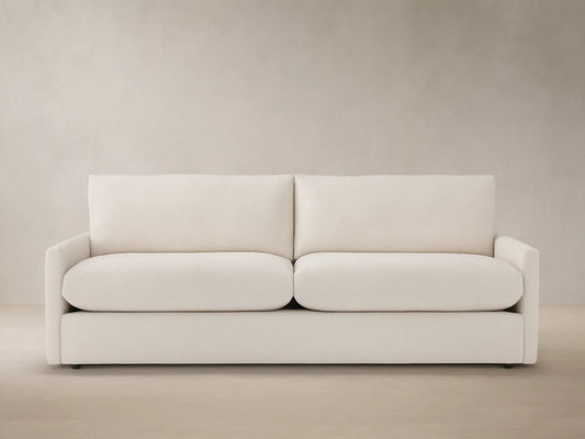Front view of Kipton Outdoor Sofa, a two-seater with off-white cushions, on a patterned patio against a light beige wall.