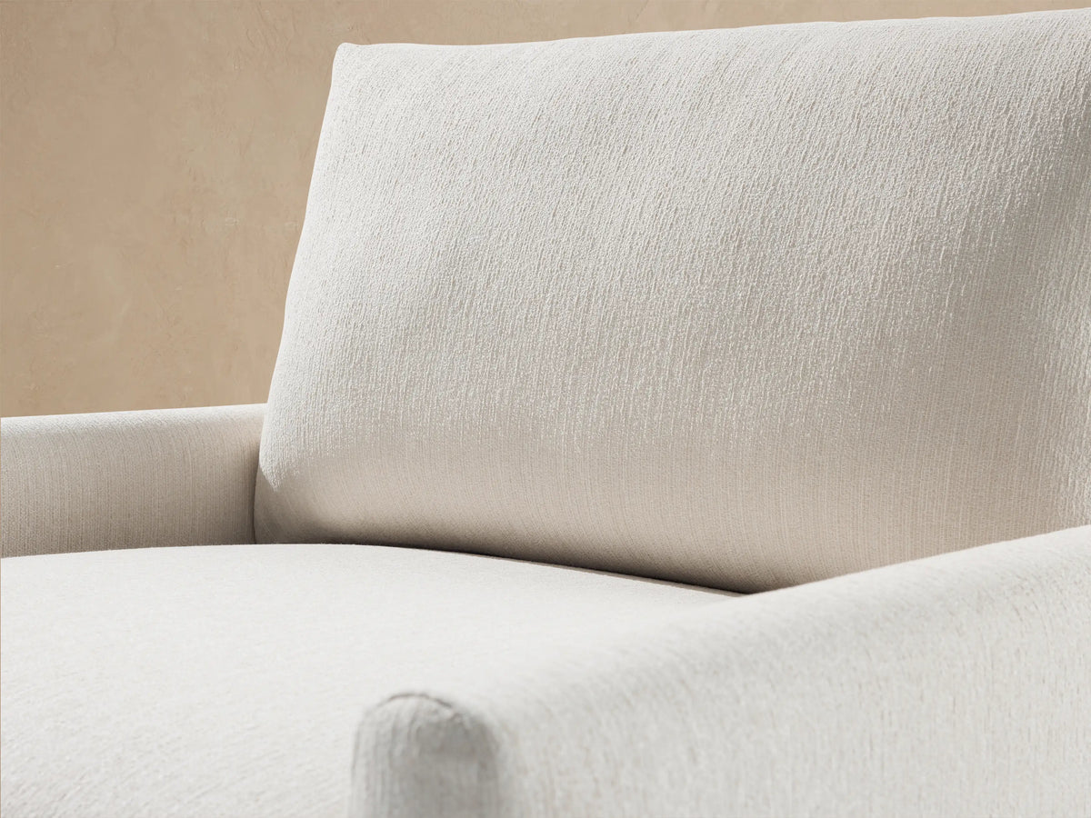 Light beige Kipton Outdoor Swivel Chair with textured fabric, padded seat & back cushions, on a stone patio against a wall.