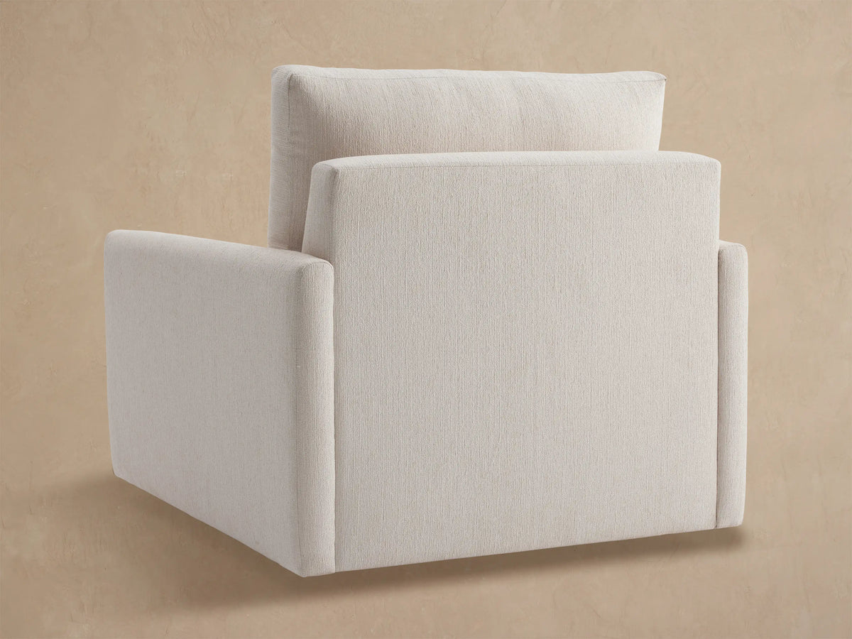 Close-up of a Kipton Outdoor Swivel Chair, showing its off-white textured back cushion, armrest, and seat against a beige wall.