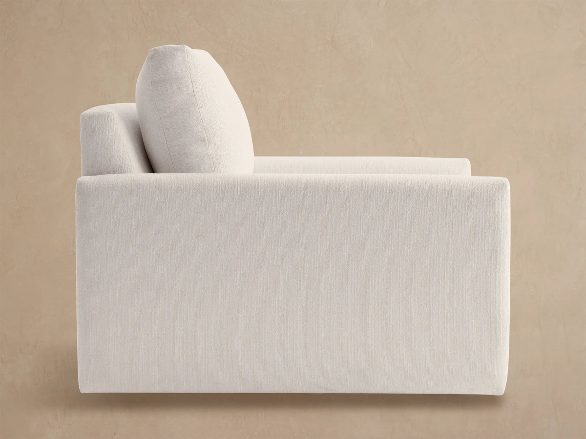 Off-white Kipton Outdoor Swivel Chair from back-right, featuring thick arms and a plush back cushion against a neutral wall.