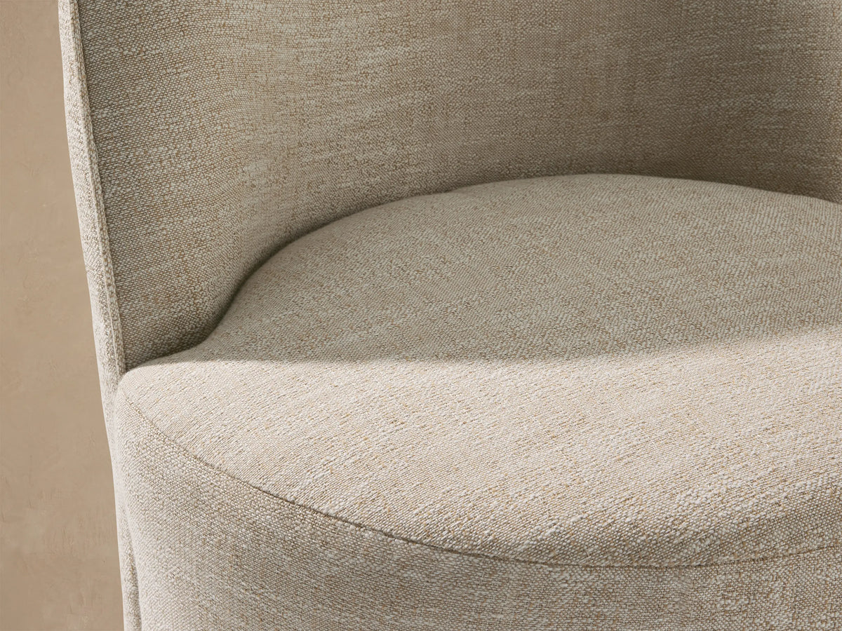 Kora Outdoor Dining Chair: Light beige upholstered chair with a rounded back and cylindrical base, sitting on a stone-tiled floor.