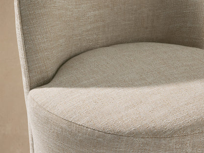 Kora Outdoor Dining Chair: Light beige upholstered chair with a rounded back and cylindrical base, sitting on a stone-tiled floor.