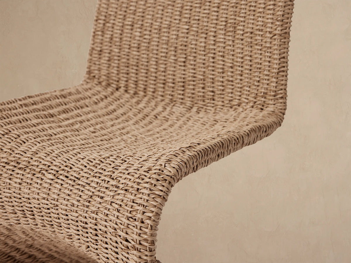 Leon Outdoor Dining Chair, front view. High-backed, armless chair crafted from textured light brown woven wicker, on a tiled floor.
