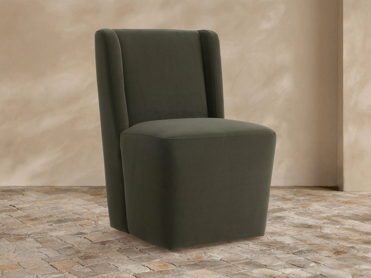 Olive green upholstered Lina Outdoor Dining Chair with high back and wide cushioned seat, on a stone floor.