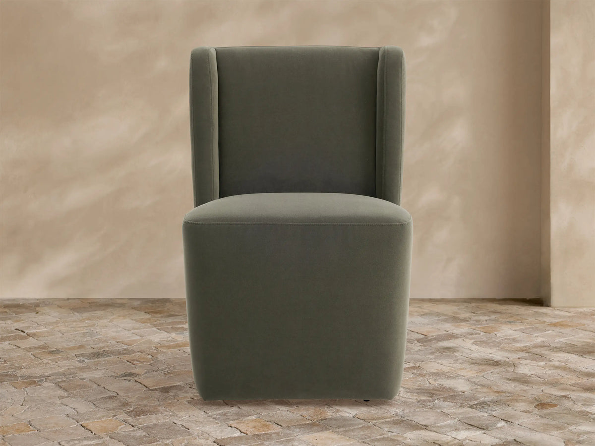 Olive green upholstered Lina Outdoor Dining Chair with high back and wide cushioned seat, on a stone floor.