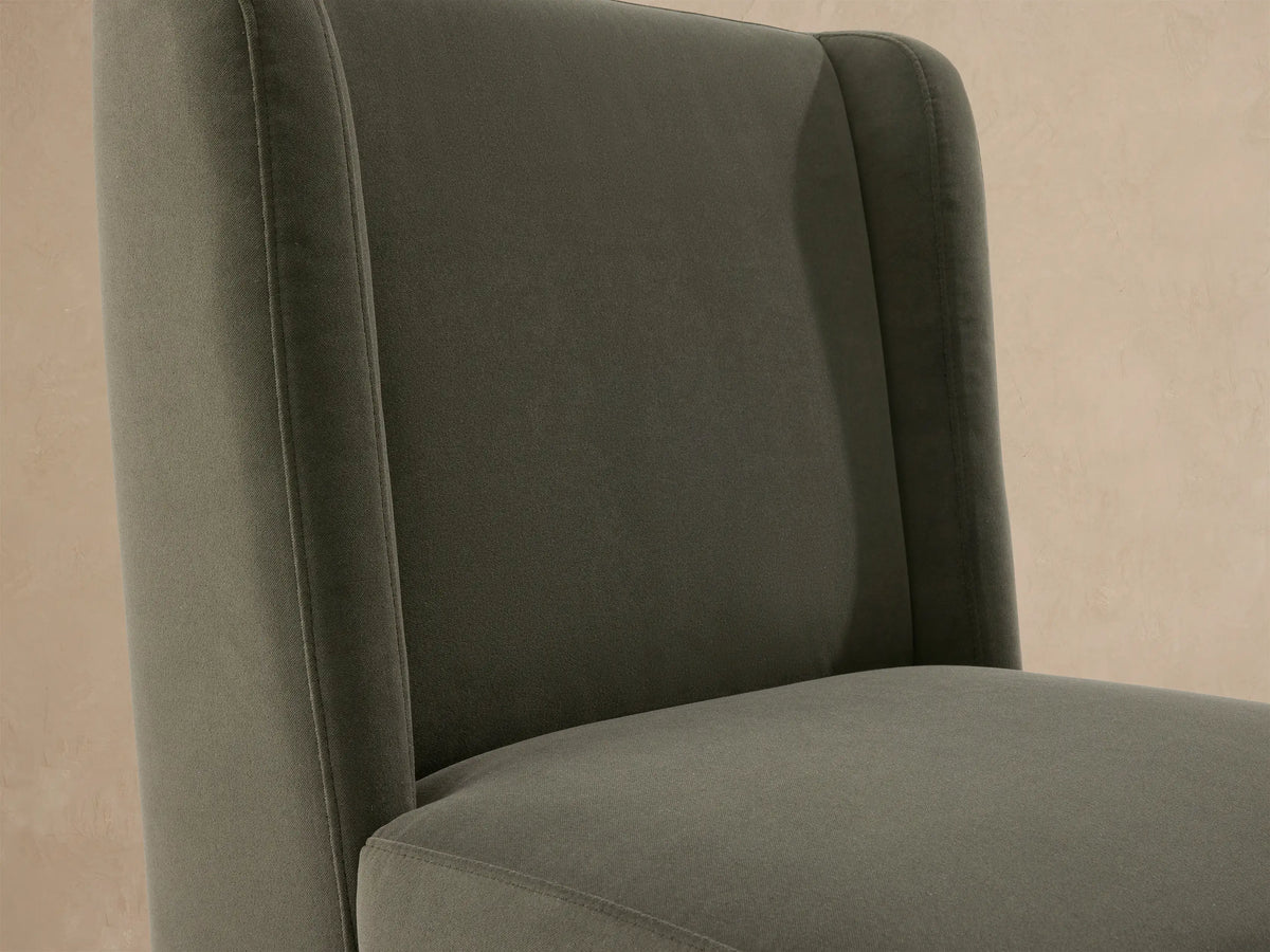 Front view of Lina Outdoor Dining Chair upholstered in muted sage green, on a textured stone floor against a beige wall.