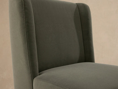 Front view of Lina Outdoor Dining Chair upholstered in muted sage green, on a textured stone floor against a beige wall.