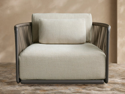 Light gray, textured Lisbon Outdoor Collection Cover on a chair, with a front seam, against a tan wall & stone patio.
