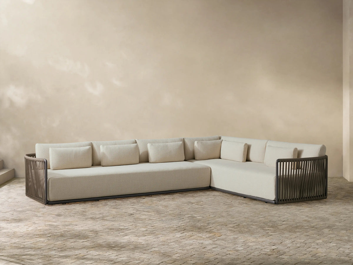 L-shaped Lisbon Outdoor Two-Piece Sectional with light beige cushions, dark woven frame, on a textured stone patio.