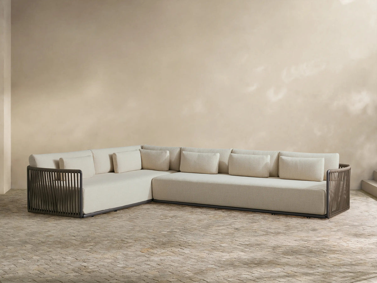 L-shaped Lisbon outdoor sectional with light beige cushions and dark woven rope frame, set on a tiled patio against a light wall.