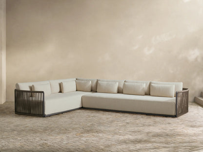 L-shaped Lisbon outdoor sectional with light beige cushions and dark woven rope frame, set on a tiled patio against a light wall.