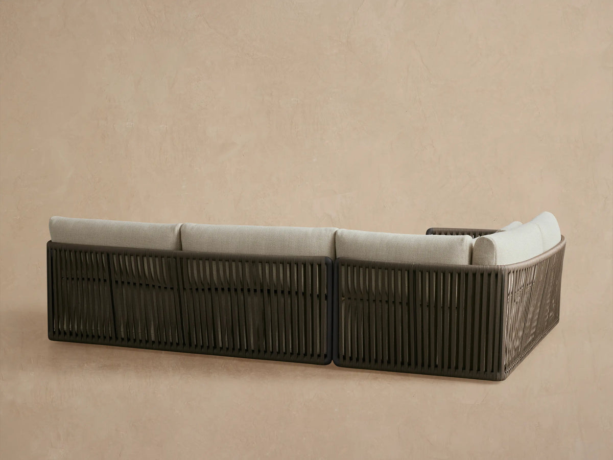 Close-up of Lisbon Outdoor Sectional's dark gray-bronze aluminum arm with olive green woven rope and beige cushions.