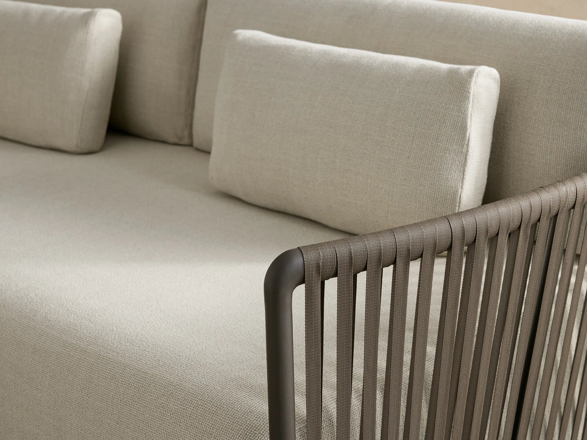 Lisbon Outdoor Sofa with light natural textured cushions & two lumbar pillows on dark woven frame, angled right on patio.