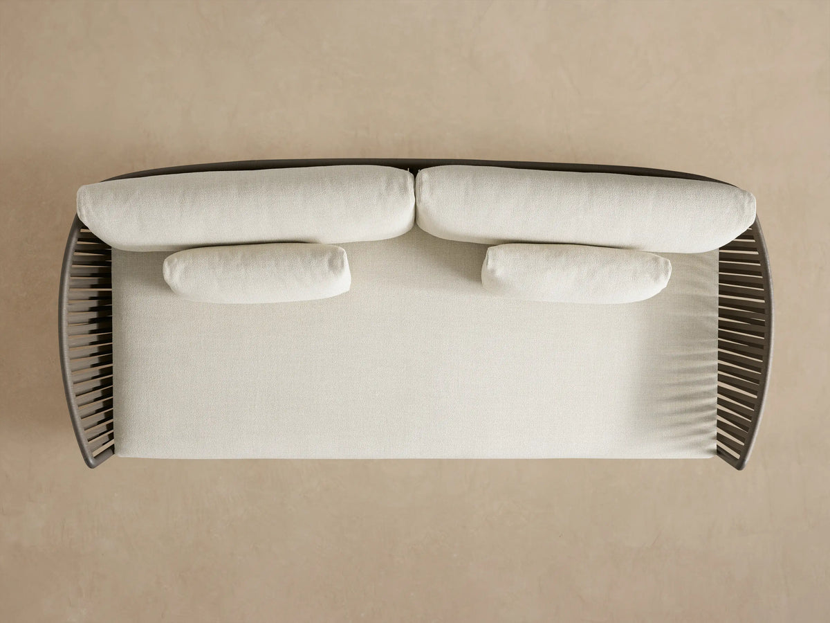 Lisbon Outdoor Sofa, back view. Dark brown woven rope frame with two light back cushions against a plain beige wall.