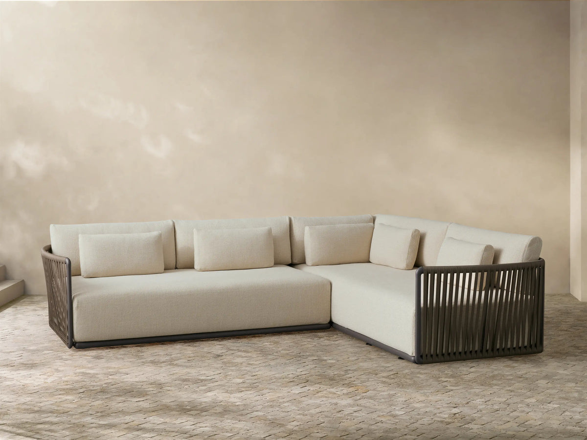 Front view of the L-shaped light beige Lisbon Outdoor Two-Piece Sectional, featuring dark brown woven rope details and accent pillows.