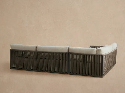 Close-up of Lisbon Outdoor Sectional showing dark gray woven rope frame, light beige cushions in soft focus behind.