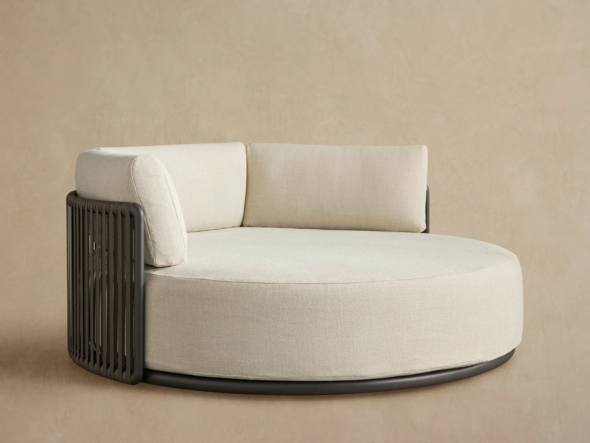Lisbon Outdoor Daybed: round, cream performance fabric seat & three back cushions on a dark aluminum frame.