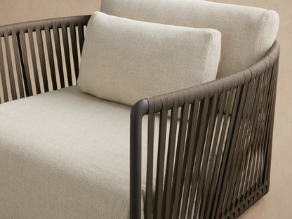 Front view of Lisbon Outdoor Swivel Chair with light beige cushions, dark gray frame, and brown woven rope arms on a patio.