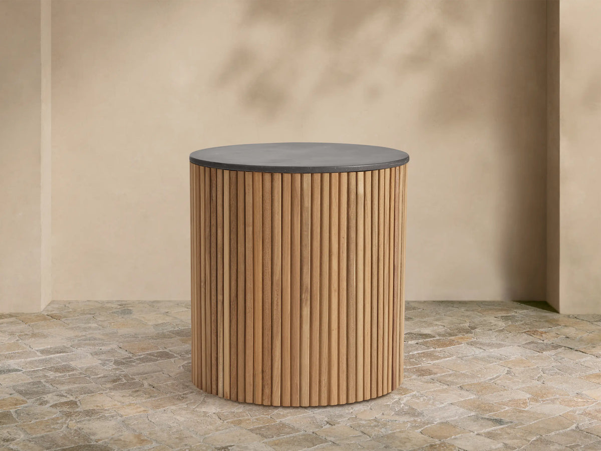 Pompeii Outdoor End Table, cylindrical, natural teak wood slatted base, dark grey concrete top, on stone patio.