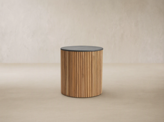 Pompeii Outdoor End Table, cylindrical, natural teak wood slatted base, dark grey concrete top, on stone patio.