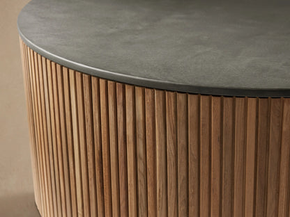 Pompeii Outdoor Round Coffee Table featuring a dark gray concrete top and cylindrical base of vertical reclaimed teak slats, on stone patio.